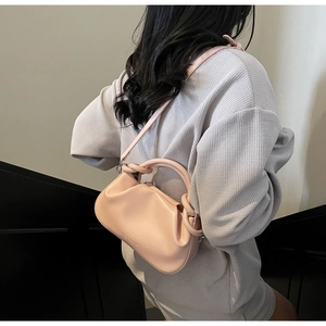 Close-up of light pink cloud bag featuring knotted handle and branded metal lettering
