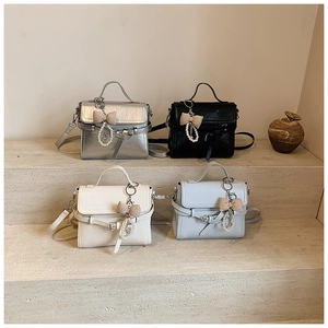Detail of four colorful leather crossbody bags with pearl bow charms on stone steps