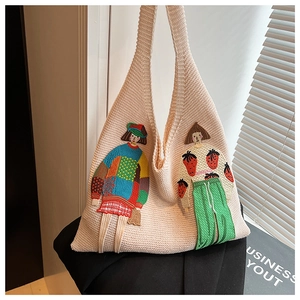 Detail der beigen Stricktasche mit bunter Cartoon-Mädchen-Stickerei und weicher Textur