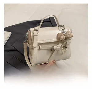 Detail of cream PU leather handbag with decorative bow, pearl charm, and flap lock buckle