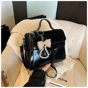 Detail of black glossy handbag featuring a bow pearl charm on a beige sofa