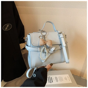 Detail of light blue crossbody bag with pearl bow charm and elegant buckle strap decoration