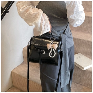 Detail of black faux leather shoulder bag with a plaid bow pearl charm and buckle