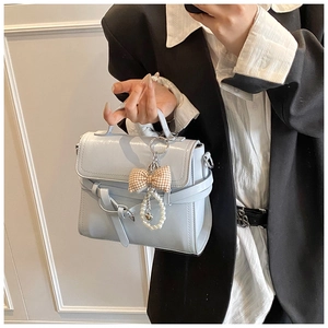 Detail of light blue square handbag with pearl bow charm and shoulder strap carried by model
