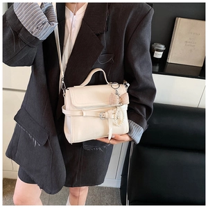 Detail view of cream crossbody bag featuring pearl chain and ribbon on a grey blazer