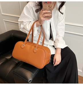 Lifestyle shot of an orange pebbled leather pillow bag held by a woman in a white shirt