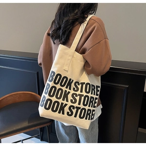 Détail du grand sac cabas en toile avec inscription bookstore porté à l'épaule