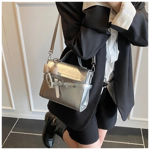 Detail of silver textured leather crossbody bag with bow pearl charm and buckle strap