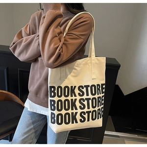 Sac fourre-tout en toile blanc cassé avec texte BOOKSTORE noir porté à l'épaule par un mannequin