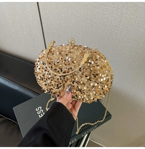 Detailed close-up of golden sequined evening clutch with crystal ball clasp and metal handles
