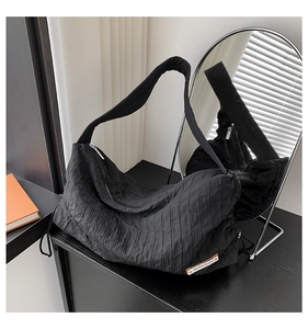 Detail of black pleated canvas tote bag featuring leather label and smooth zipper