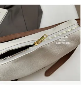 Detail of smooth gold metal zipper and lychee pattern leather on white dumpling bag