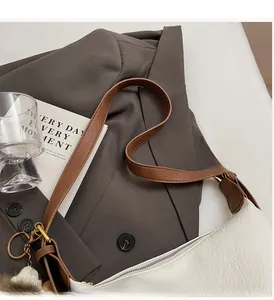 Close-up of white lychee leather dumpling bag with brown strap and white pompom charm