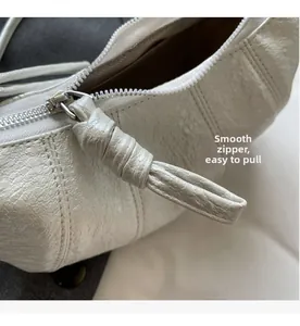 Macro detail of a white croissant bag showing the smooth metal zipper and pleated texture