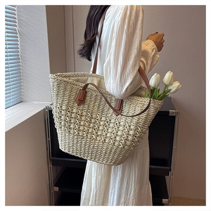 Detail of a beige woven tote bag with brown leather handles worn by a model in a white dress
