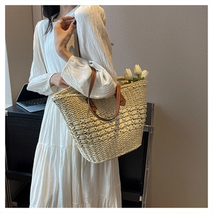 Detail of woven straw tote bag with brown leather handles and reinforced metal rivets