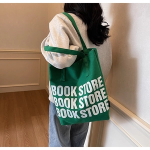 Détail du sac fourre-tout en toile verte avec texte BOOK STORE porté à l'épaule par un modèle