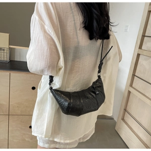 Close-up of black glossy crackle texture croissant bag with knotted shoulder strap detail