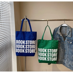 Détail de sacs cabas en toile bleus et verts avec impression lettrage Book Store blanc