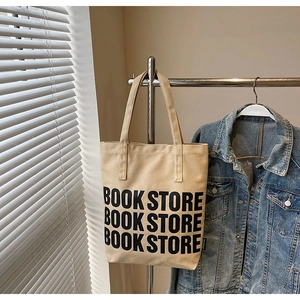 Détail du sac cabas en toile beige avec texte Book Store suspendu à côté d'une veste en jean