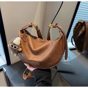 Detail view of brown pebbled leather crescent bag featuring a cute plush toy pendant charm