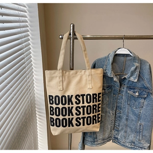 Gros plan du sac cabas en toile beige avec inscription BOOK STORE et veste en jean