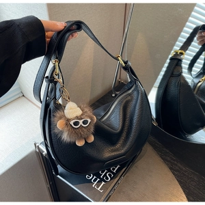 Detail of black pebbled leather hobo bag with gold hardware and plush monster charm