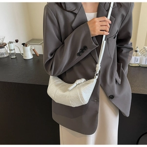 Close-up of white croissant bag showing textured pleated faux leather and knotted strap