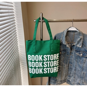 Détail du sac cabas en toile verte avec lettrage BOOK STORE accroché à un support