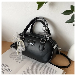 Detailed view of a black bowling handbag with pearl lace bow and checkered ribbon on a desk