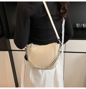 Detail of cream saddle bag with chunky silver chain strap and glossy finish in lifestyle setting