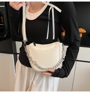 Close-up of a cream chain handbag with silver metal link and adjustable strap on a model
