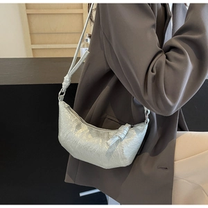 Silver metallic pleated croissant bag with knotted strap detail shown on a grey blazer