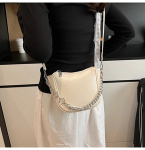 Close-up of cream saddle bag with silver moon chain detail and adjustable strap on model
