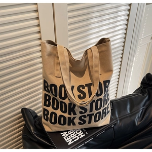 Détail d'un sac cabas en toile kaki avec imprimé BOOK STORE posé sur un canapé en cuir