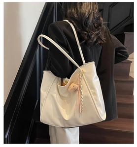 Detail einer großen cremefarbenen Hobo-Tasche mit Bärenanhänger, von Model getragen