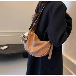Close-up of caramel hobo bag featuring pebbled texture and plush doll charm