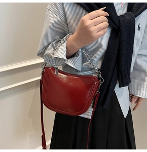 Deep red patent leather saddle bag detail with silver chain strap and zip closure