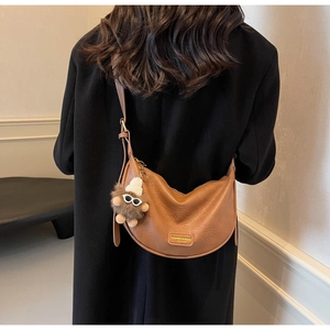 Detailed shot of brown textured leather crescent bag with cute plush bear pendant accessory