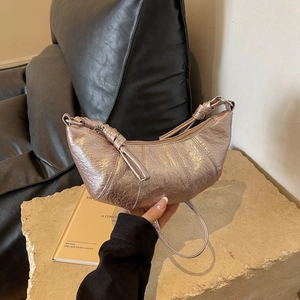 Detailed close-up of metallic rose gold crescent bag with textured pleats and knot handle