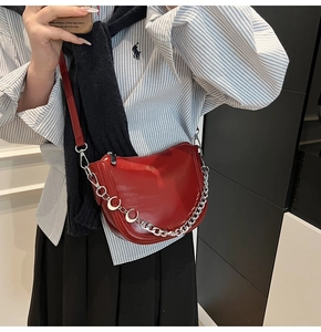 Detail of red glossy patent leather saddle bag with chunky chain and crescent buckle