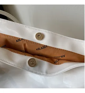 Detail einer weißen Lackleder-Tasche mit Magnetverschluss und gravierten Metallbeschlägen