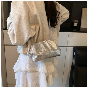 Silver metallic cloud bag with snake texture and chain strap worn by a model
