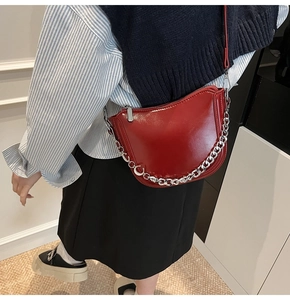 Close-up of bright red patent leather saddle bag with chunky silver chain strap and zipper