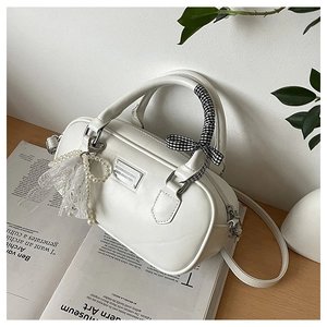Detail of white bowling bag with pearl charm and checkered ribbon on wooden table