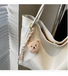 Nahaufnahme von süßem Plüschbär-Anhänger mit Quaste an einer weißen Ledertasche