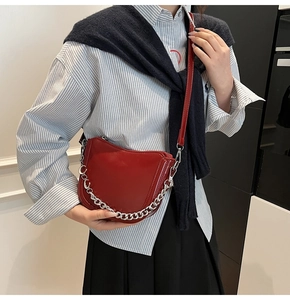 Detailed macro view of the glossy red saddle bag with decorative silver chain strap