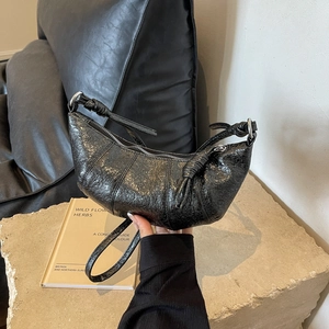 Close-up of black pleated patent leather crossbody bag with knot detail and silver hardware