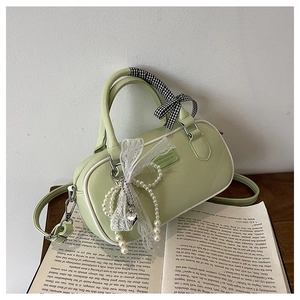 Detail of light green barrel bag with ribbon handle and pearl heart charms on a book
