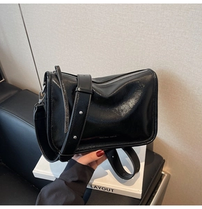 Détail du sac bandoulière noir brillant avec large bandoulière et fermeture éclair en métal
